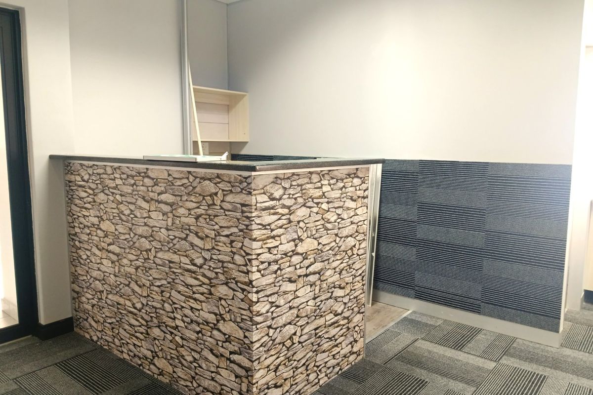 A commercial office space featuring a built-in reception desk with stone-effect cladding and modular carpet tile flooring.