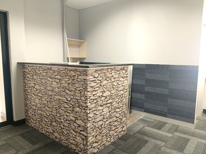 A commercial office space featuring a built-in reception desk with stone-effect cladding and modular carpet tile flooring.