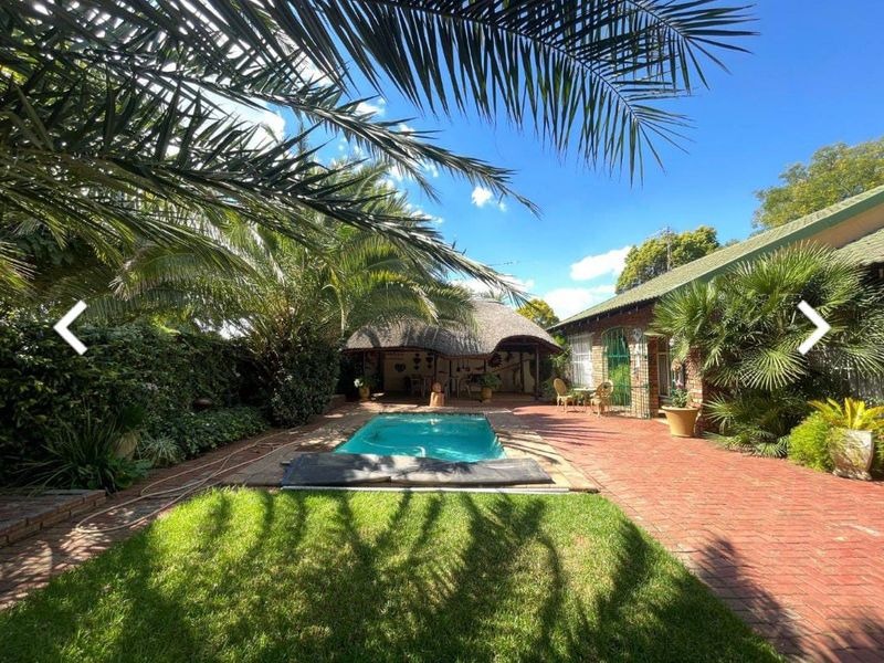 A private outdoor pool area featuring a thatched lapa, brick paving, and established garden surroundings, ideal for relaxation and outdoor entertainment.