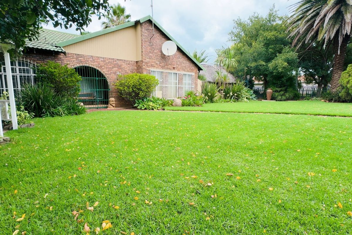 A well-maintained rear garden featuring a lush green lawn, established landscaping, and a brick-built home with security features.