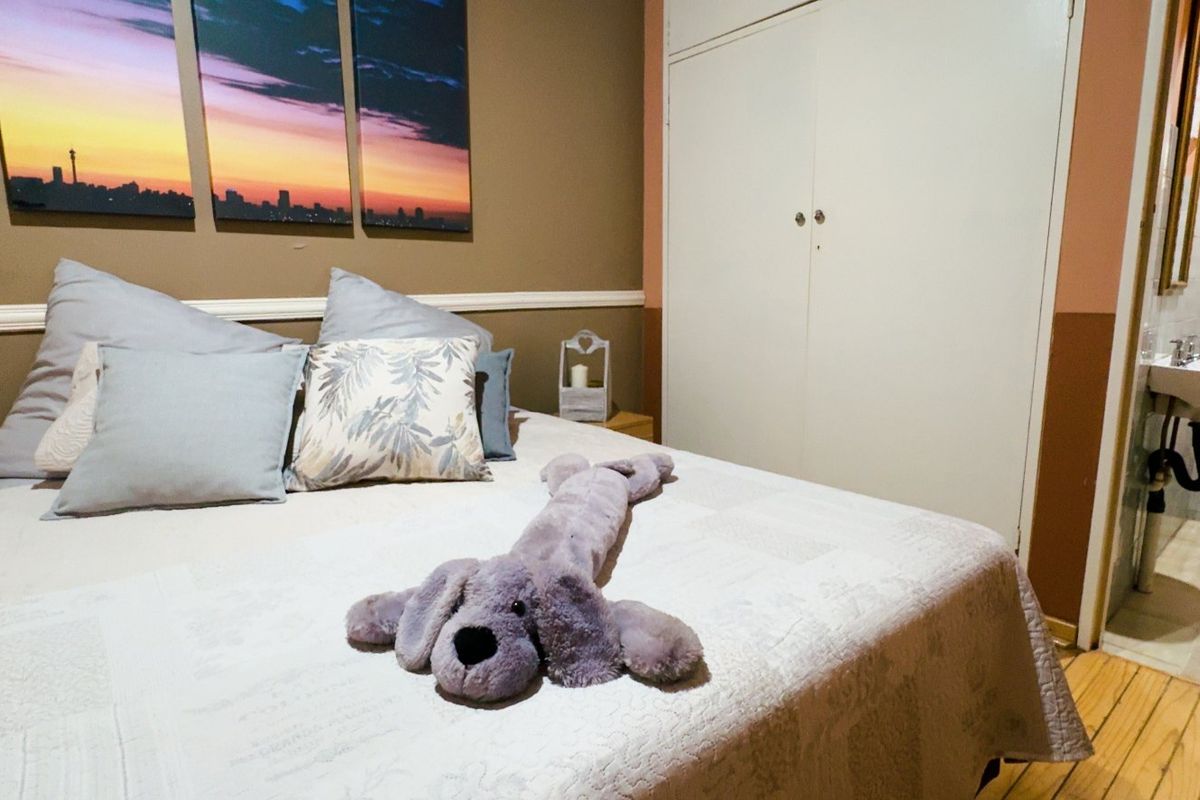A bedroom featuring wooden flooring, a built-in wardrobe, and an attached en-suite bathroom with a toilet and pedestal basin.