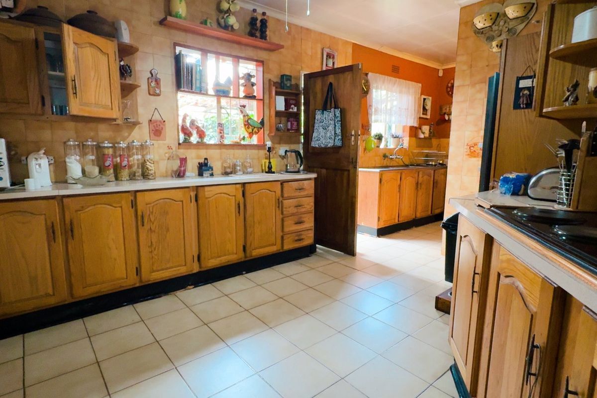 A spacious kitchen featuring traditional wooden cabinetry, tiled backsplash, and tiled flooring, offering a functional layout with ample storage and counter space.