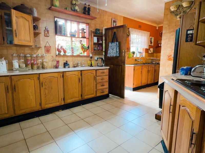 A spacious kitchen featuring traditional wooden cabinetry, tiled backsplash, and tiled flooring, offering a functional layout with ample storage and counter space.