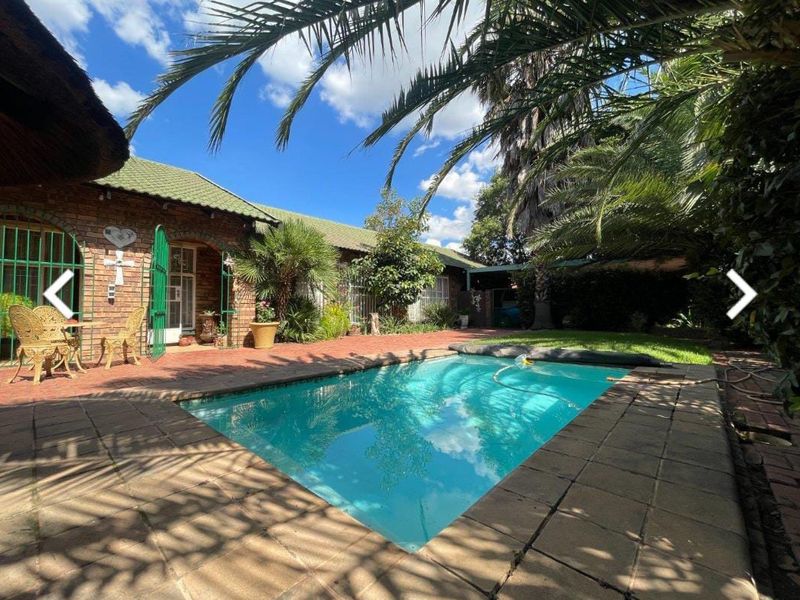 Outdoor pool area featuring a swimming pool, brick paving, and a covered patio area with a thatched roof.