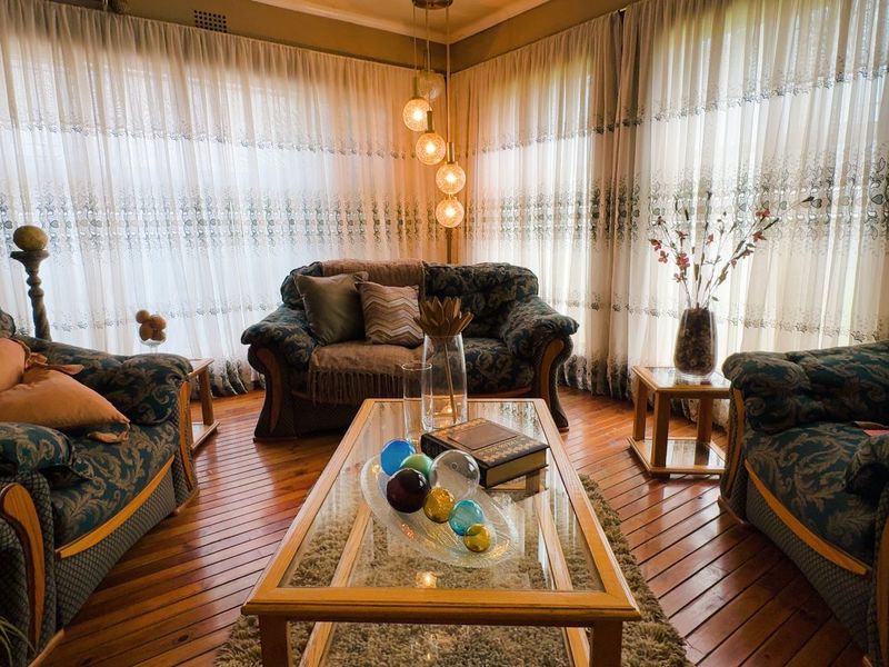 A cozy living room featuring warm hardwood flooring, large windows with sheer curtains, and a modern pendant light fixture.