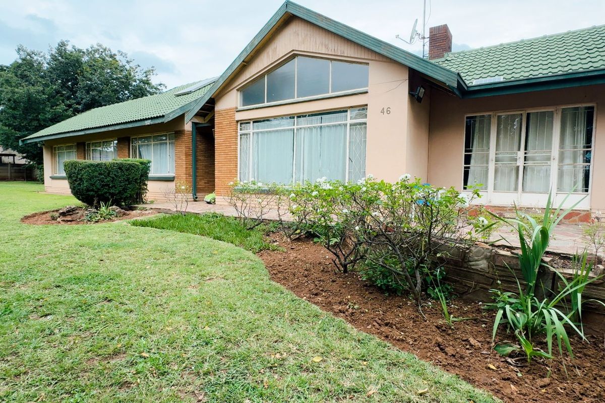 Rear view of a single-story house featuring a paved patio, stone retaining wall, and a large gabled window overlooking a spacious garden.