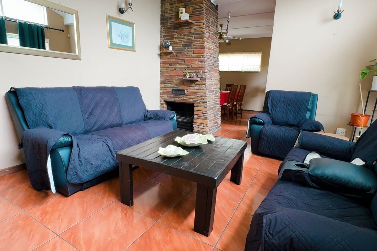 A living room featuring a central brick fireplace and tiled flooring, with an open-plan flow leading into the adjacent dining area.