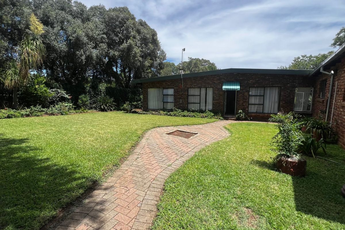 A well-maintained rear garden featuring a brick-paved pathway leading to the house, surrounded by established trees and a neat lawn.
