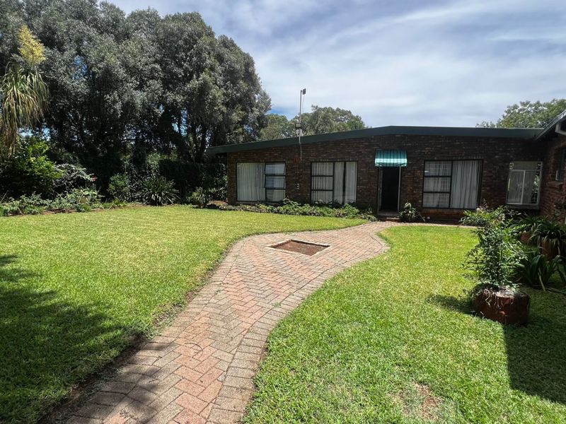 A well-maintained rear garden featuring a brick-paved pathway leading to the house, surrounded by established trees and a neat lawn.