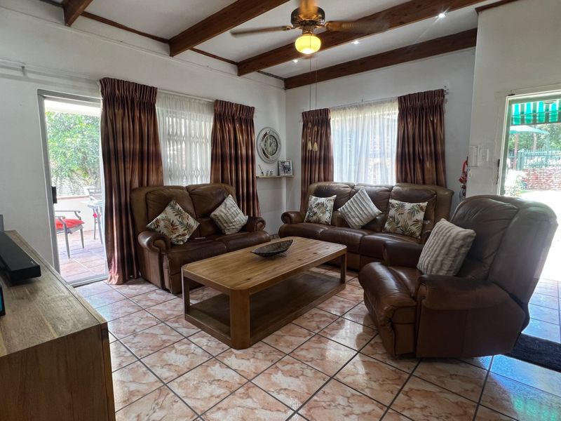 Spacious living room featuring exposed timber ceiling beams, tiled flooring, and direct access to the outdoor patio area through sliding glass doors.