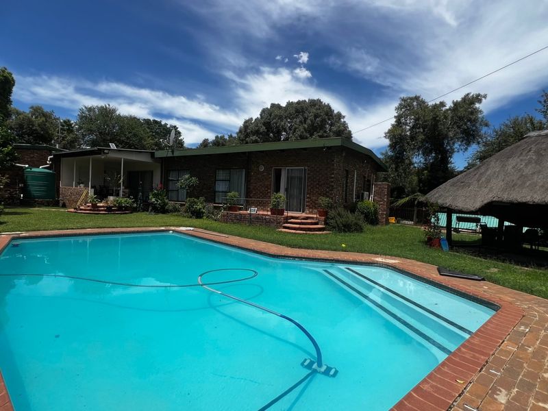 A spacious backyard featuring a swimming pool, brick-paved surround, and a traditional thatch lapa, perfect for outdoor entertaining.