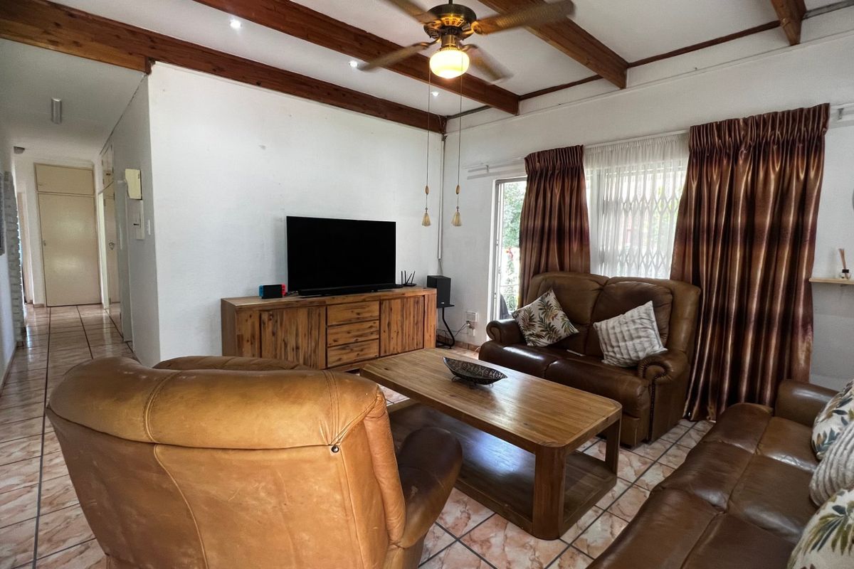 A living room featuring exposed timber ceiling beams, a ceiling fan, and tiled flooring, providing a comfortable and functional space.
