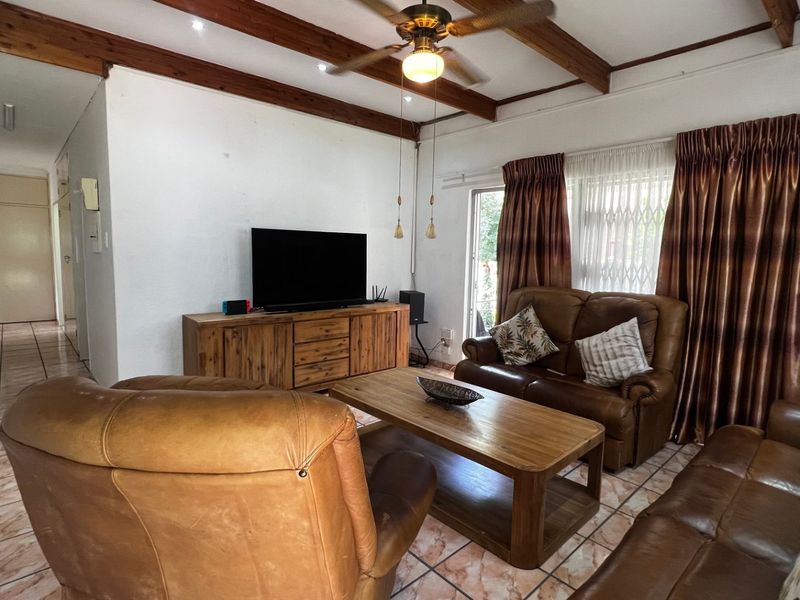A living room featuring exposed timber ceiling beams, a ceiling fan, and tiled flooring, providing a comfortable and functional space.
