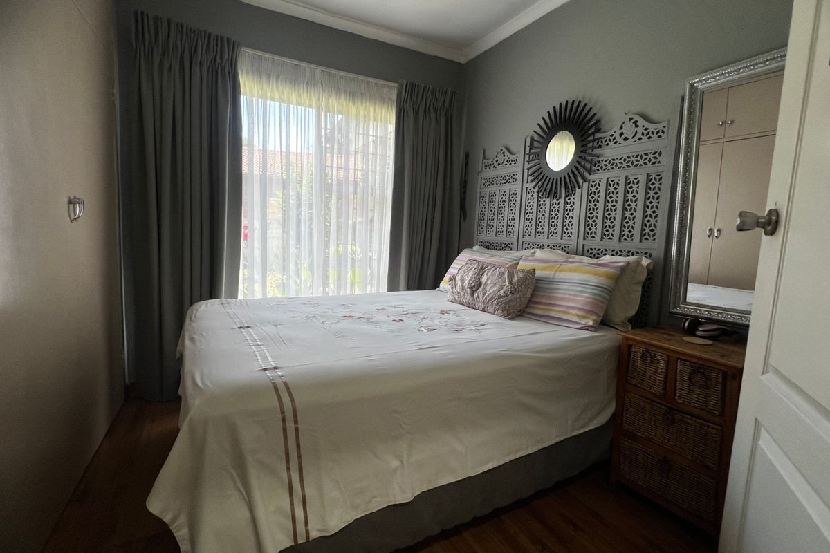 A well-maintained bedroom featuring laminate flooring, built-in cupboards, and large windows with curtain tracks, offering a comfortable and functional living space.