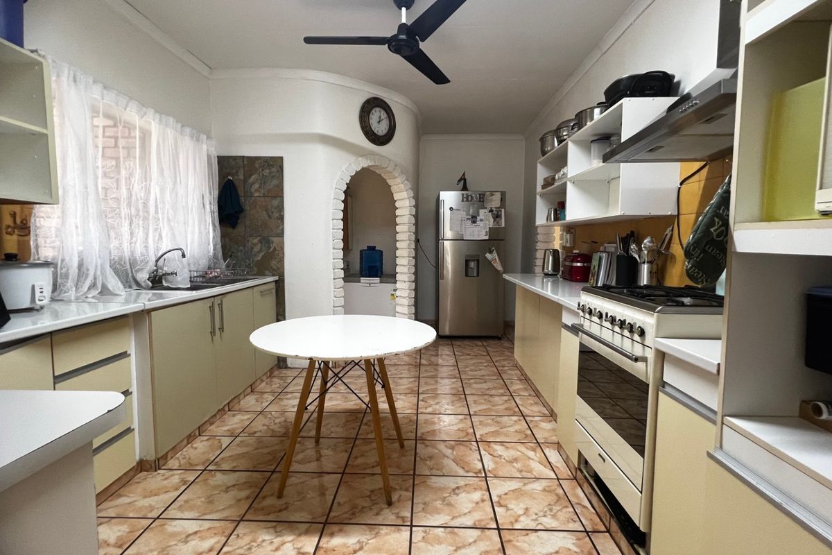 A functional kitchen featuring built-in cabinetry, a gas stove with extractor fan, double sink, and tiled flooring, accented by a unique arched doorway.