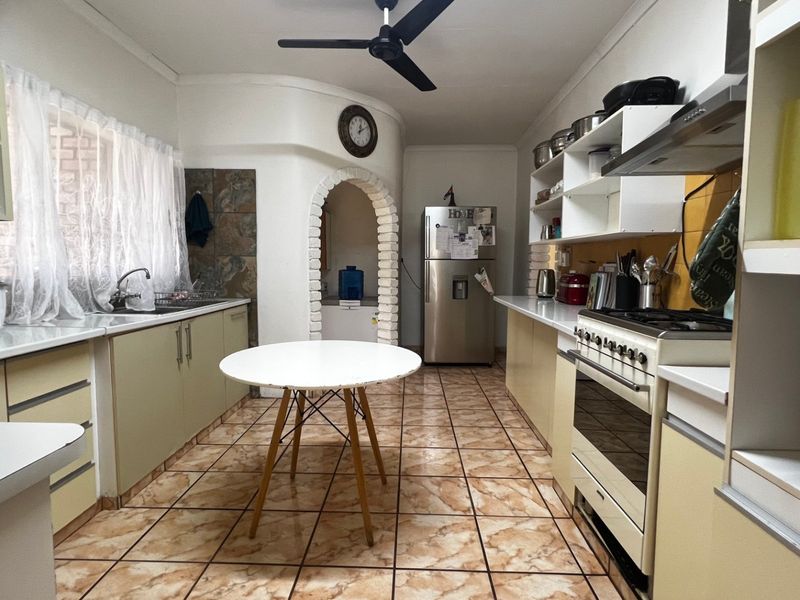 A functional kitchen featuring built-in cabinetry, a gas stove with extractor fan, double sink, and tiled flooring, accented by a unique arched doorway.