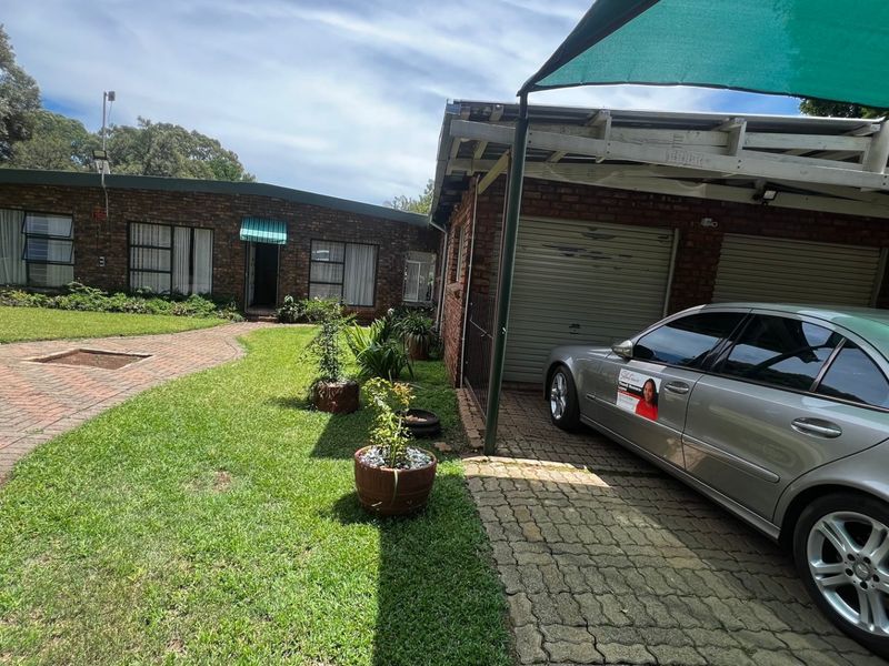 Front exterior view of a brick house featuring a paved driveway, lawn, and a covered carport area with garage access.