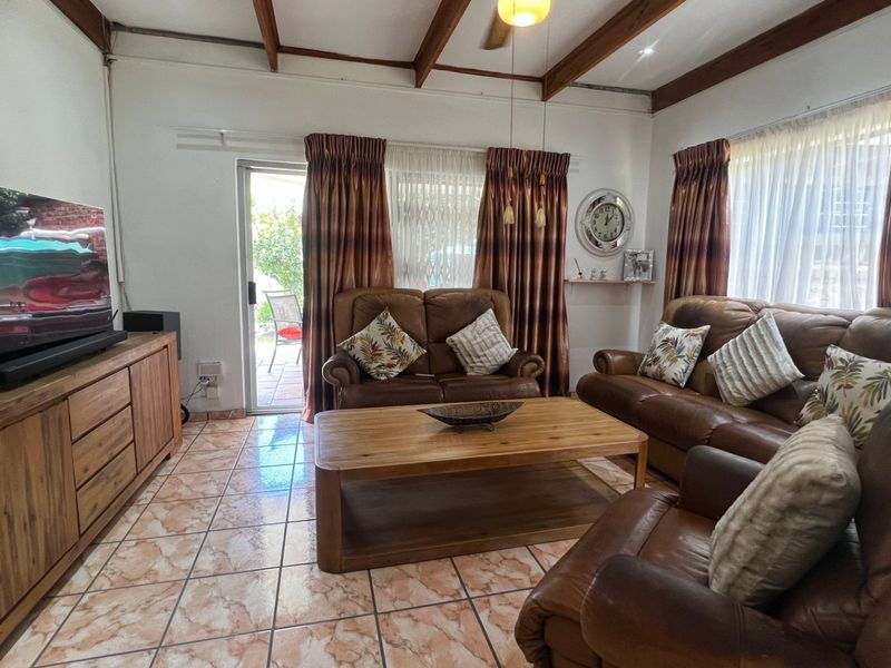 A comfortable living room featuring exposed timber ceiling beams, tiled flooring, and a sliding glass door providing direct access to the outdoor patio area.