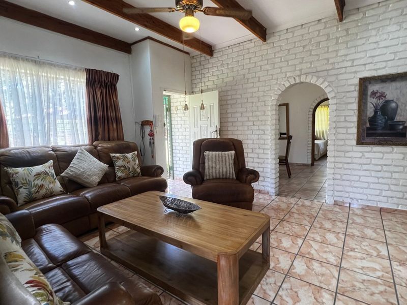 Spacious living room featuring exposed timber ceiling beams, a painted brick feature wall, and an arched entryway leading to adjacent rooms.