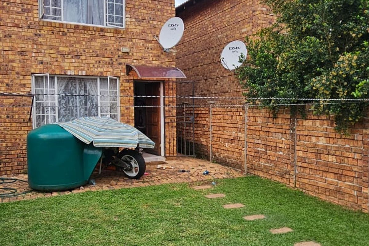 Rear view of a double-story face brick house featuring a small paved patio, lawn, and boundary wall.