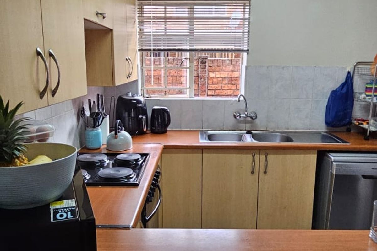 Functional kitchen featuring light wood-tone cabinetry, laminate countertops, a stainless steel double sink, and a built-in hob with tiled splashback.
