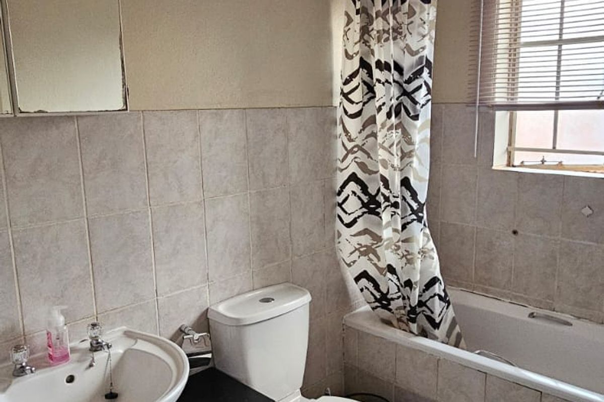 A functional bathroom featuring a pedestal basin, toilet, and a bathtub with a shower curtain, finished with neutral wall and floor tiling.