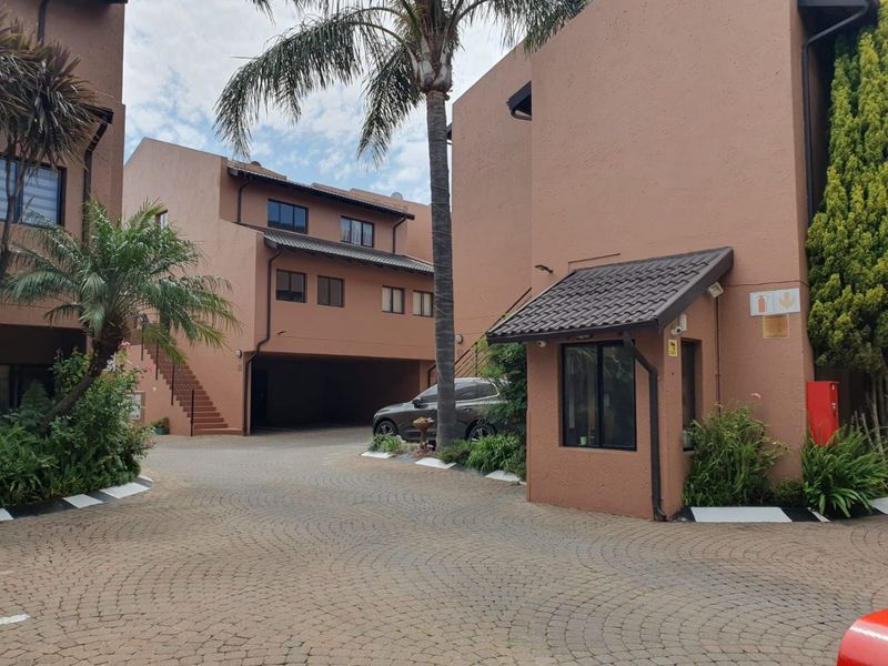 Front entrance view of the apartment complex featuring a paved driveway, security guard house, and multi-story residential buildings with tiled roofs.