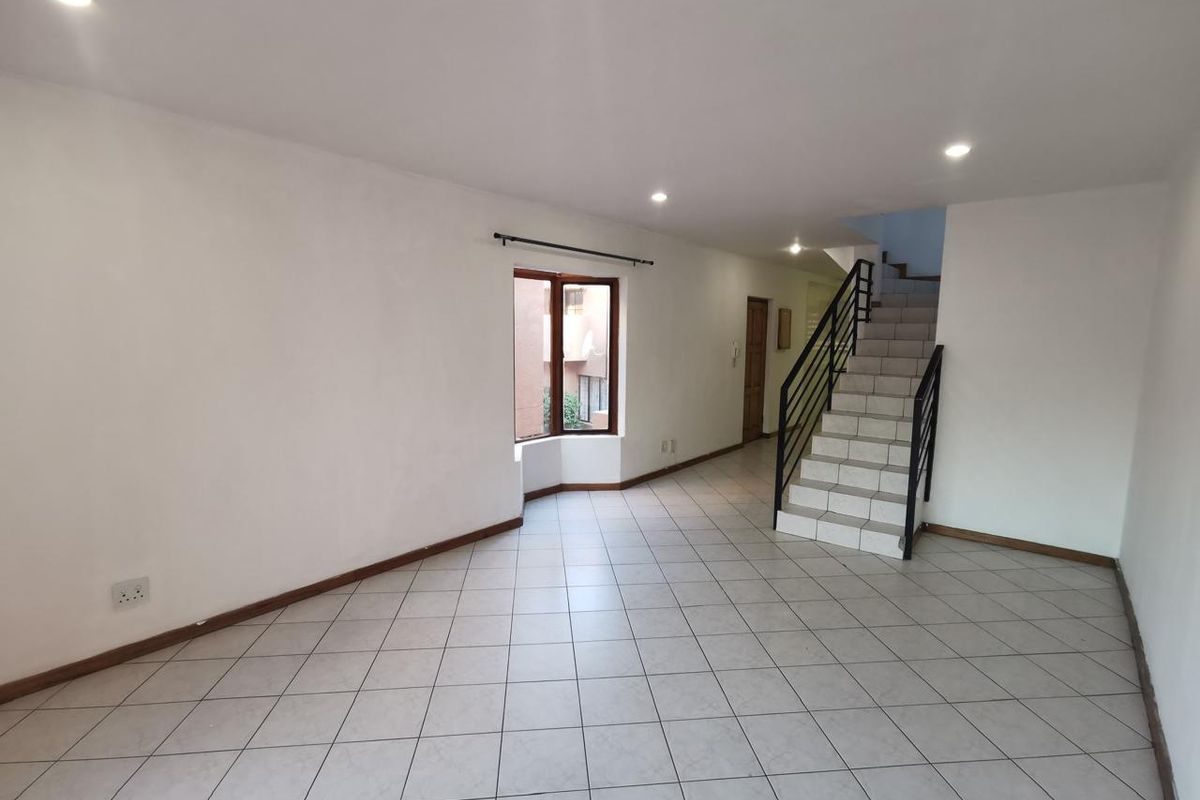 An open-plan living area featuring tiled flooring, recessed lighting, and a staircase with a metal railing leading to the upper level.