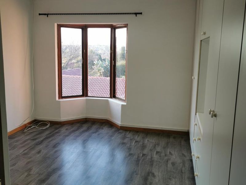 A bright, empty bedroom featuring modern laminate flooring, a large bay window, and extensive built-in cupboard storage.