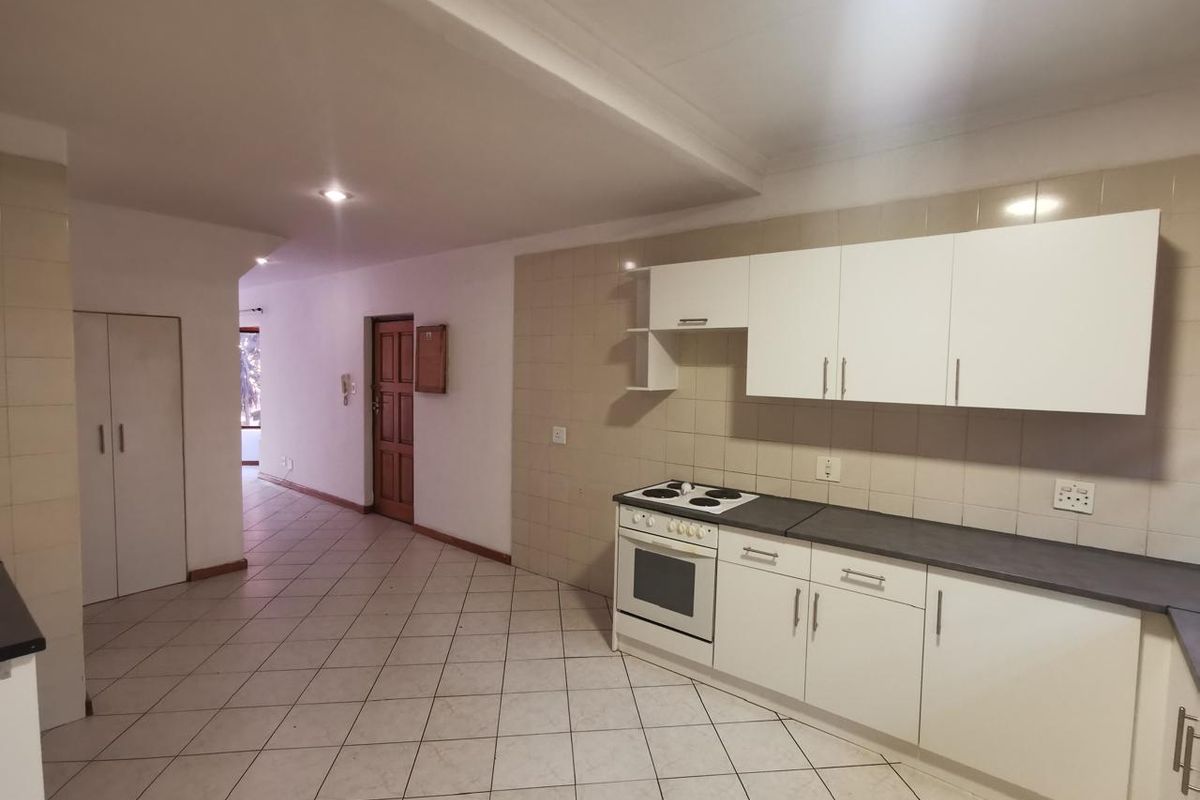 A functional kitchen featuring white cabinetry, an electric stove with oven, tiled backsplash, and neutral floor tiles, leading into an open hallway area.
