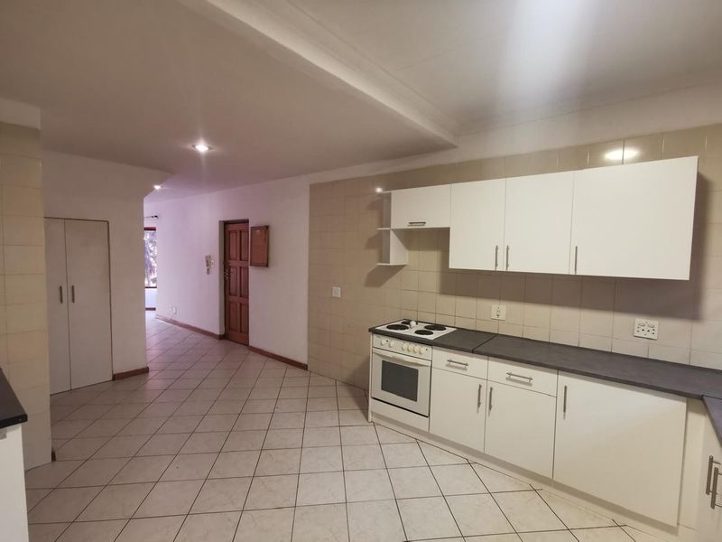 A functional kitchen featuring white cabinetry, an electric stove with oven, tiled backsplash, and neutral floor tiles, leading into an open hallway area.