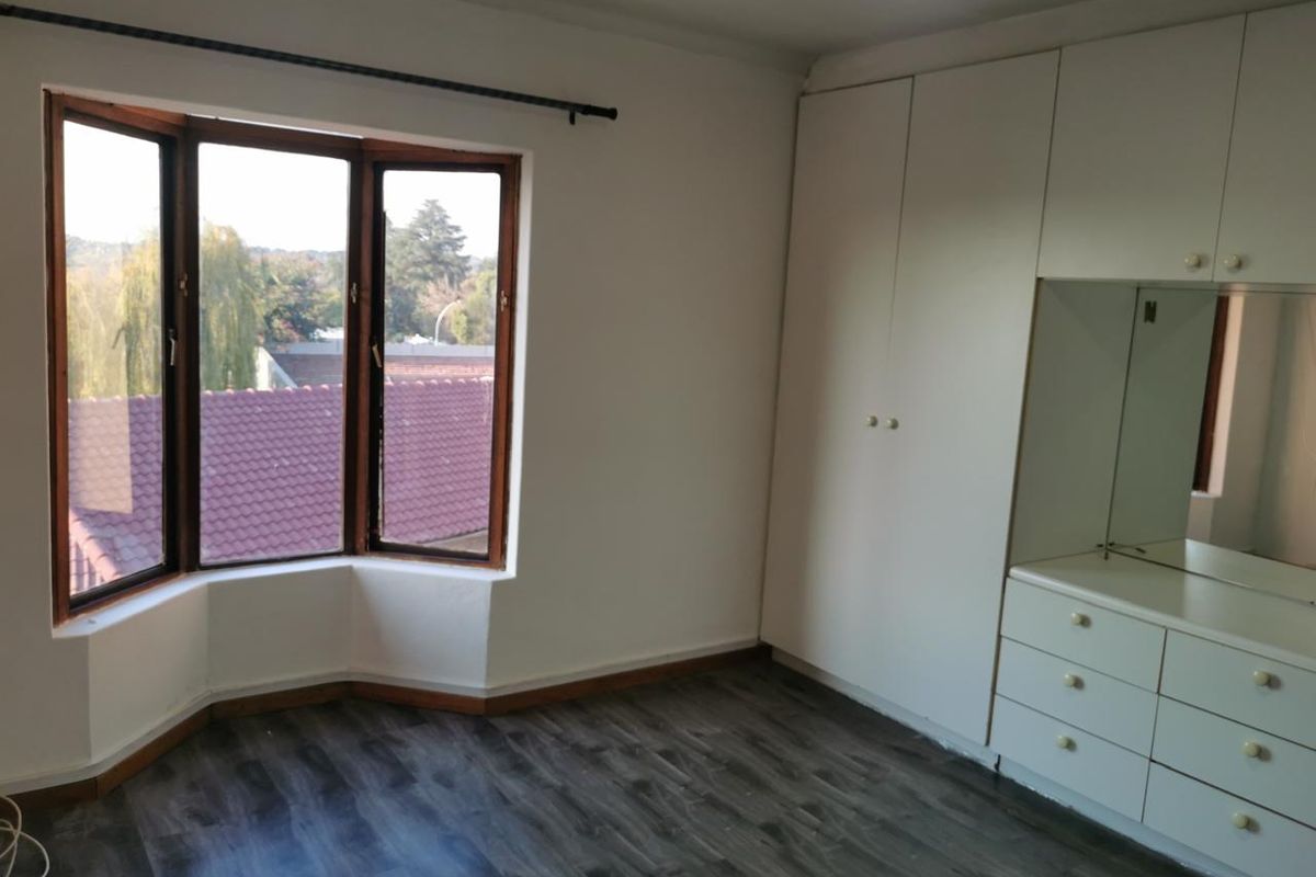 A bright, empty bedroom featuring laminate flooring, a large bay window, and extensive built-in cabinetry with an integrated vanity area.
