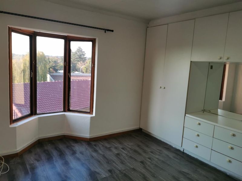 A bright, empty bedroom featuring laminate flooring, a large bay window, and extensive built-in cabinetry with an integrated vanity area.