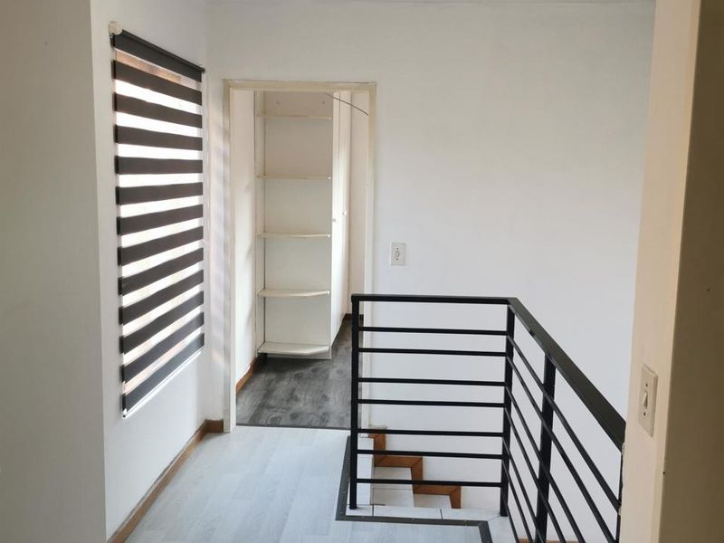 A bright, modern hallway featuring light laminate flooring, a sleek metal staircase balustrade, and built-in shelving in the adjacent alcove.