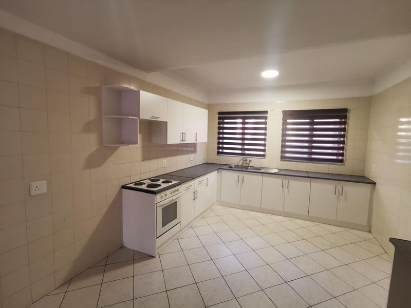A functional kitchen featuring white built-in cabinetry, an electric stove with oven, double sink, and tiled finishes throughout.