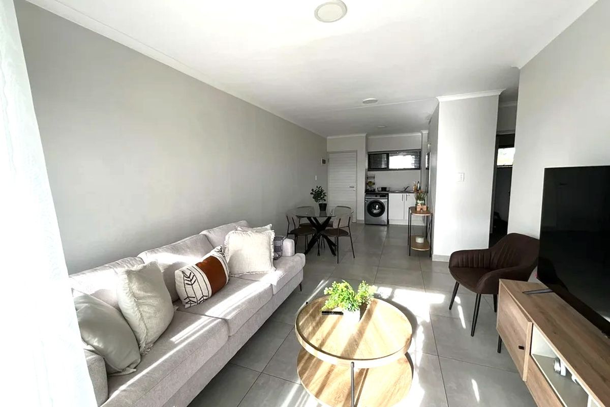 Bright open-plan living area featuring neutral tiled flooring, recessed lighting, and a compact kitchen space with integrated laundry facilities.