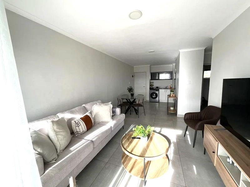 Bright open-plan living area featuring neutral tiled flooring, recessed lighting, and a compact kitchen space with integrated laundry facilities.
