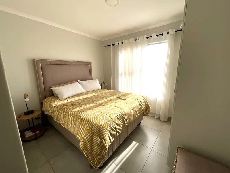 A well-lit bedroom featuring neutral wall tones and tiled flooring, providing a clean and comfortable living space.