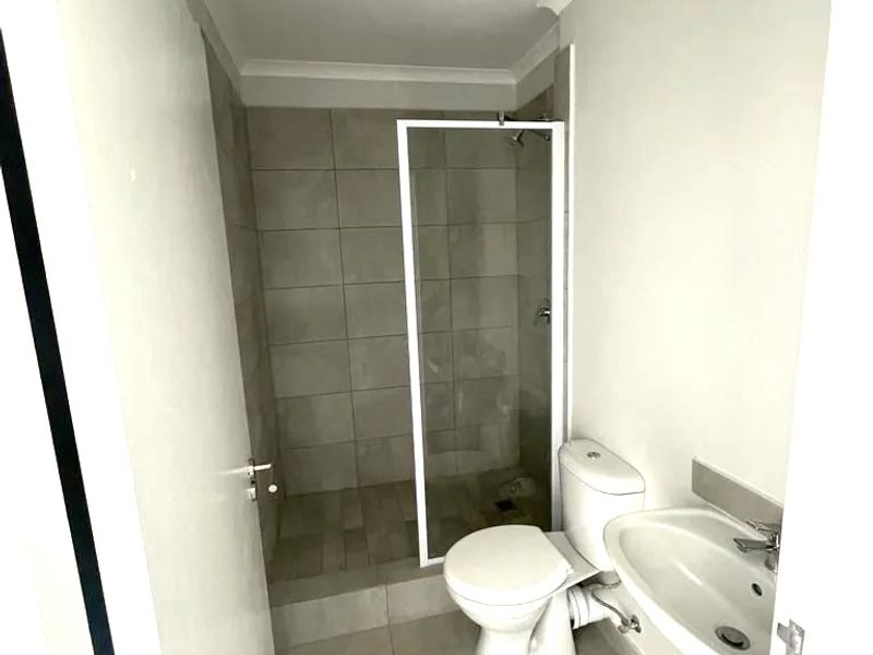 A clean, modern bathroom featuring a walk-in shower with glass enclosure, a white toilet, and a wall-mounted basin with neutral floor and wall tiling.