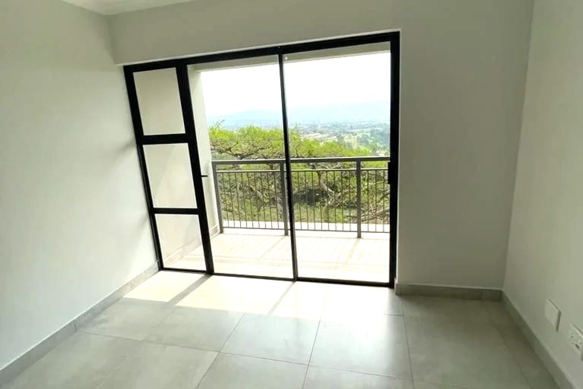 A bright, empty bedroom featuring large sliding glass doors that open onto a private balcony with scenic views and modern tiled flooring.