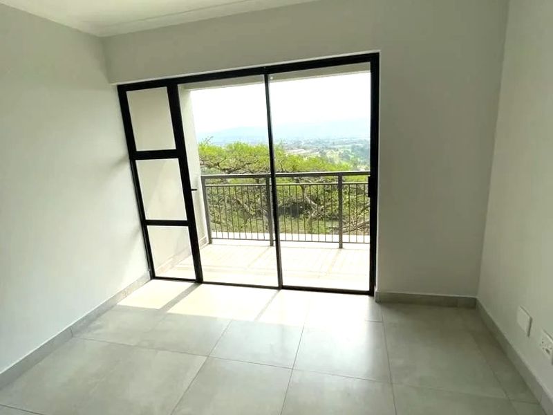 A bright, empty bedroom featuring large sliding glass doors that open onto a private balcony with scenic views and modern tiled flooring.