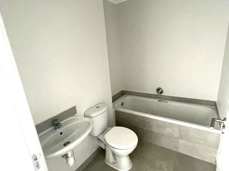 A clean, modern bathroom featuring a bathtub, pedestal basin, and toilet with neutral grey floor tiles and white walls.