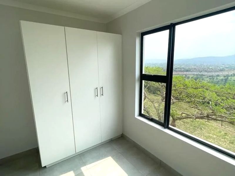 A bright, empty bedroom featuring modern tiled flooring, a built-in wardrobe, and a large window offering scenic landscape views.