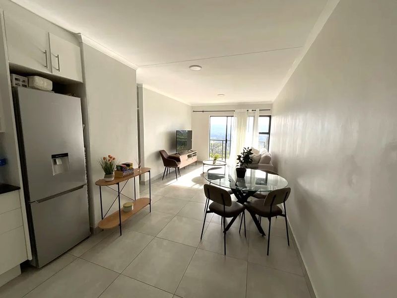 Bright open-plan living and dining area featuring neutral tiled flooring, recessed lighting, and direct access to a balcony with scenic views.