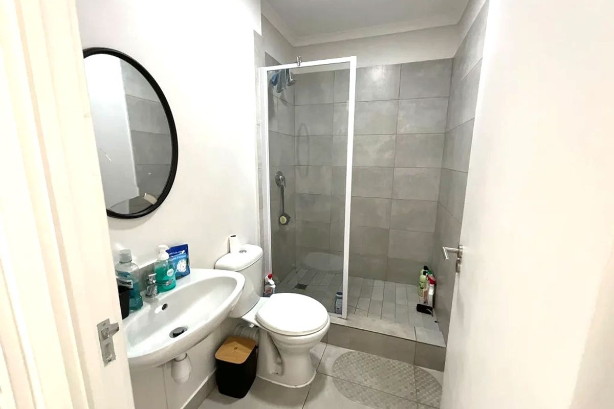A functional bathroom featuring a walk-in shower with glass enclosure, wall-mounted basin, and neutral floor-to-ceiling tiling.