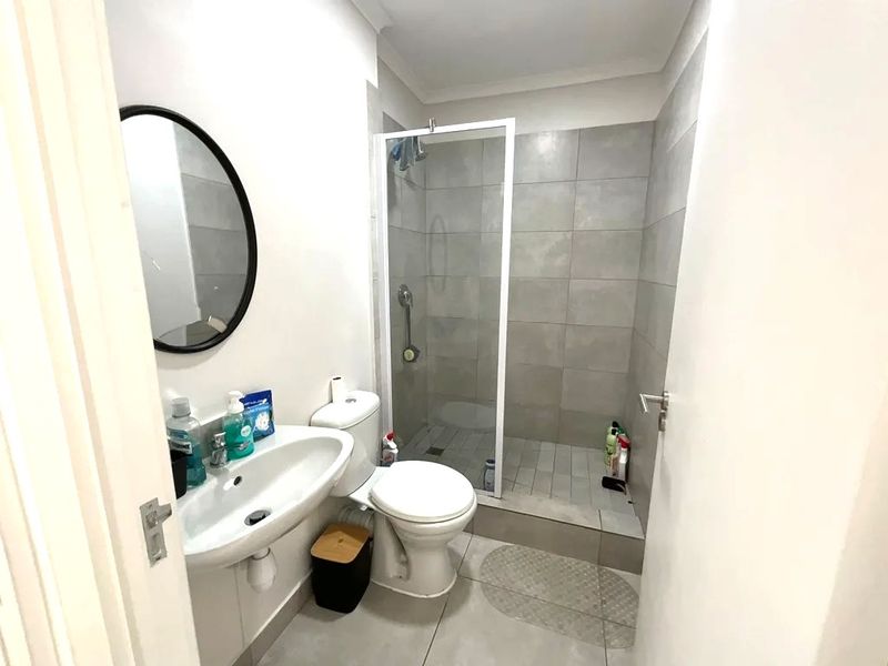 A functional bathroom featuring a walk-in shower with glass enclosure, wall-mounted basin, and neutral floor-to-ceiling tiling.