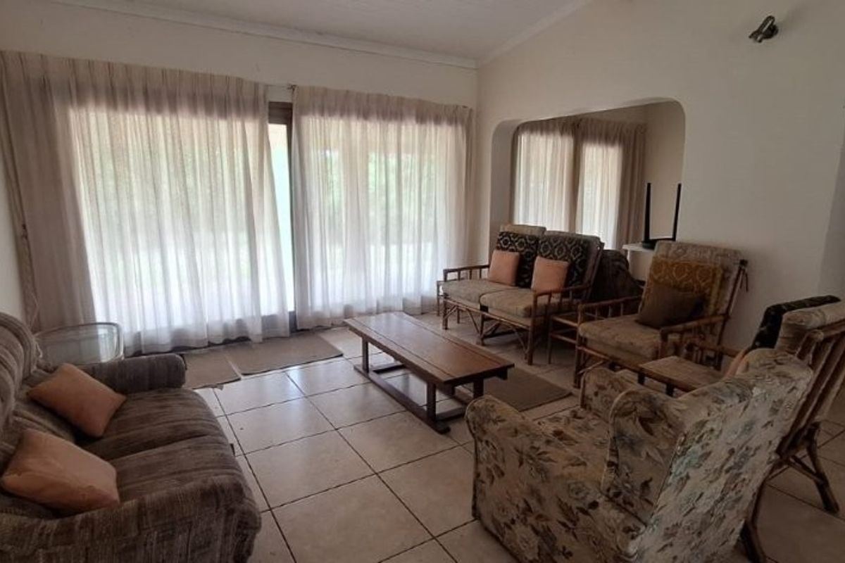 A spacious living room featuring tiled flooring, large sliding glass doors for natural light, and an open archway leading to adjacent areas.