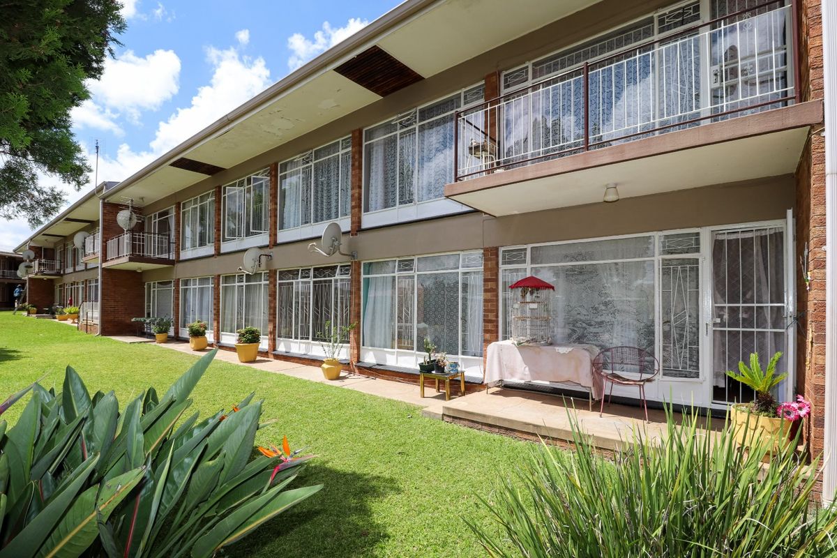 Rear view of a multi-story apartment building featuring brick facade, ground floor patio access, and upper-level balconies overlooking a shared lawn area.