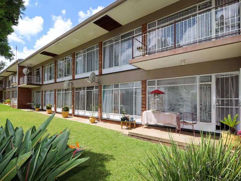 Rear view of a multi-story apartment building featuring brick facade, ground floor patio access, and upper-level balconies overlooking a shared lawn area.