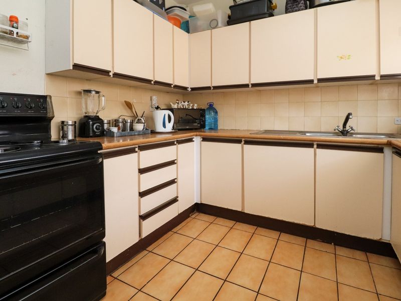 A functional kitchen featuring laminate countertops, tiled backsplash, ceramic flooring, and ample built-in cabinetry, offering a dated aesthetic ready for modernization.